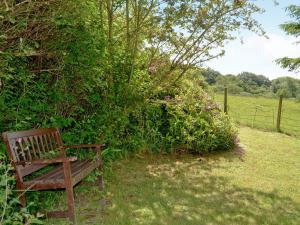 a wooden bench sitting in the grass next to a bush at Whortleberry Cottage in Wheddon Cross