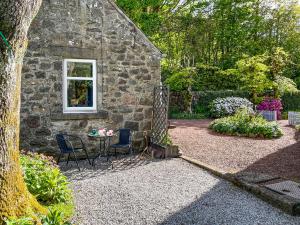 a stone building with a table and chairs in a garden at Craigrannoch Cottage in Rockcliffe