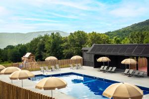 a pool with umbrellas and chairs with mountains in the background at Huttopia Berkshires in Hancock