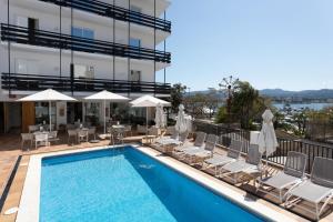 a pool with chairs and umbrellas next to a building at Es Mitjorn Hotel in San Antonio