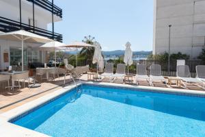 a swimming pool with chairs and umbrellas next to a building at Es Mitjorn Hotel in San Antonio
