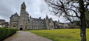 a large stone building with a grass field in front of it at Glen Mor Apartment with pool on site in Fort Augustus