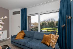 a blue couch in a living room with a large window at Welcome in - Appartement aan de duinen met balkon I Duinweg 18, Zoutelande 'Duinroos' in Zoutelande