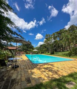 a swimming pool with a table and an umbrella at Pousada Arara in Valença