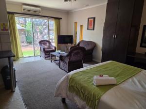a bedroom with a bed and chairs and a living room at Sekelbos Guesthouse in Pretoria