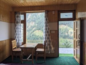 a room with a table and chairs and a large window at Jibhi Emberwood in Jibhi