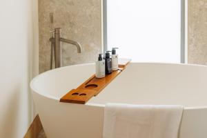 a white bath tub with bottles on it in a bathroom at Rena's Retreat - Luxury Architectural Eco Home with hot tub a short walk from Gurnard in Cowes - Perfect Lux Stay for Sailers Couples and Older Families in Gurnard +42 photos