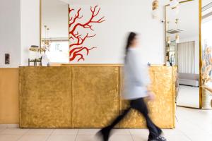 a woman walks past a store with a sign on the wall at Coral Hotel - Hotelia Hospitality Group in Ierapetra