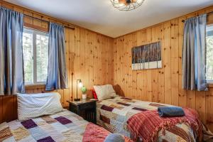 two beds in a room with wooden walls at Riverfront Cabin w/ Hot Tub in Schroon Lake! in Schroon Lake