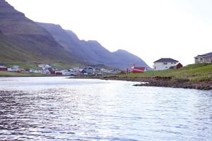a river with houses and mountains in the background at FjordNest Cabin in Hvannasund