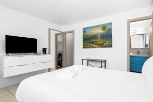 a white bedroom with a bed and a tv at Private Studio w Pool Patio steps to the Beach in Deerfield Beach