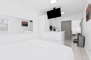 a white bedroom with a white bed and a flat screen tv at Private modern studio w pool - Steps to the beach in Deerfield Beach