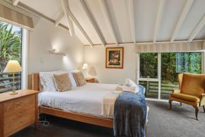a bedroom with a bed and a chair and windows at Waitati Retreat in Waitati