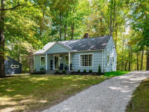 a white cottage in the woods with a driveway at Renovated Cottage - Game Room - Fire Pit - Sleeps 8 in Moreland Hills