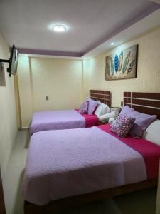 two beds in a hotel room with purple sheets at HOTEL PUEBLO BONITO in Zacatlán
