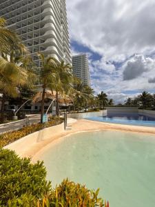 a swimming pool with palm trees and a tall building at Cloud Haven Suite at Azure North Pampanga in San Fernando