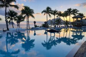 a pool with palm trees and the ocean at sunset at 412 The Diamond Swing in Le Diamant