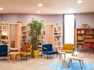 a waiting room with chairs and tables and bookshelves at greet Hotel Rennes Pace in Pacé