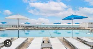 a swimming pool with blue umbrellas and the ocean at Ocean front Condo with balcony on the beach in Sunny Isles Beach