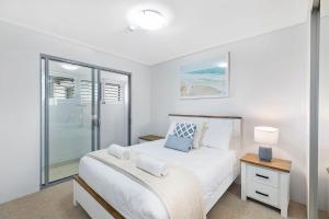 a white bedroom with a bed and a glass door at Coast Apartments 19 Roof Top Pool in The Entrance +5 photos