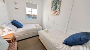 a room with two beds with blue pillows and a window at The Gunyah by Experience Jervis Bay in Huskisson
