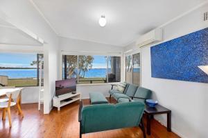 a living room with a couch and a tv at Lakes Edge Cottage Pet Friendly Waterfront Escape in Budgewoi