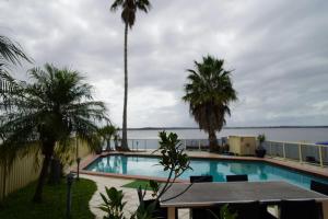 a swimming pool with palm trees and the water at Toukley Waterfront House in Toukley