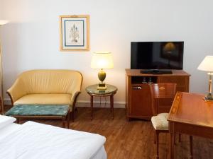 a hotel room with a tv and a couch and a chair at DORMERO Hotel Halle in Halle an der Saale +12 photos