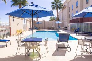 a pool with tables and chairs and blue umbrellas at Hampton Inn & Suites Blythe, CA in Blythe
