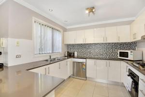 a white kitchen with white cabinets and a window at The Gallipoli Residence in Long Jetty +4 photos