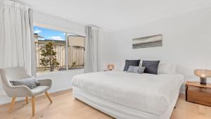 a white bedroom with a bed and a chair and a window at 21 Forever in Pokolbin +10 photos