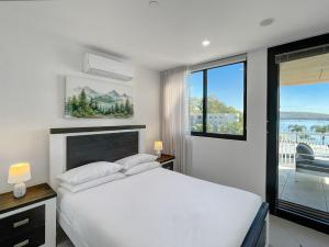 a white bedroom with a bed and a large window at Bay View 2-Bedroom Apartment in Batemans Bay