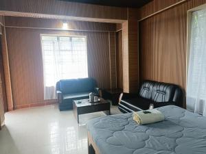 a bedroom with a bed and a couch and chairs at Streamside Guest House in Mawlynnong