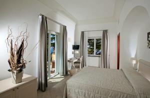 a white bedroom with a bed and a desk and a mirror at Hotel Villa Ceselle in Anacapri