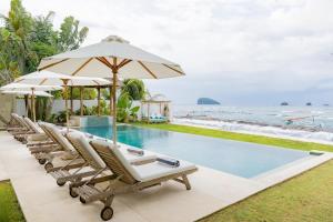 a pool with chairs and an umbrella and the ocean at Villa Oceana, Candidasa in Candidasa