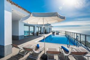 una piscina con sillas y una sombrilla en el balcón en Villa São Lourenço, en Fajã da Ovelha