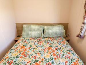 a bed with a floral comforter and two pillows at Sunflower Retreat, Caravan 61 in Morpeth