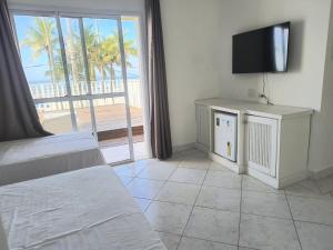 ein Schlafzimmer mit Bett, Fernseher und Balkon in der Unterkunft Jequitiba Hotel Frente ao Mar in Guarujá