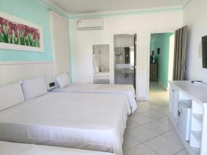 ein weißes Zimmer mit zwei Betten und einem Badezimmer in der Unterkunft Jequitiba Hotel Frente ao Mar in Guarujá + 54 Fotos