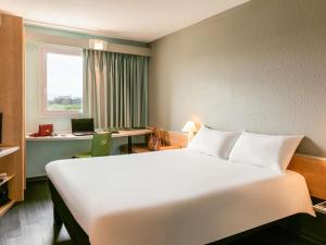a hotel room with a large white bed and a desk at ibis Auch in Auch +66 photos