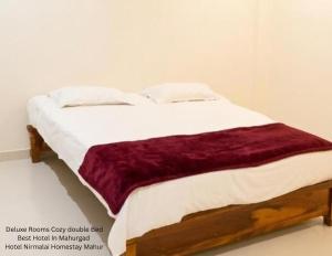 a bed in a white room with a burgundy blanket at Hotel Nirmalai Palace Mahur in Māhūr