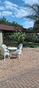 three white chairs and a table in a park at Meltz Inn in Klerksdorp