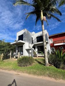 a white house with a palm tree in front of it at Suíte completa com cozinha e hidromassagem in Torres