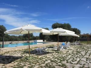 two white umbrellas and chairs next to a swimming pool at Masseria Montecchie in Ceglie Messapica
