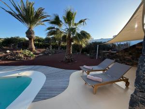 a swimming pool with two lounge chairs and palm trees at Casa Bagus in Lajares