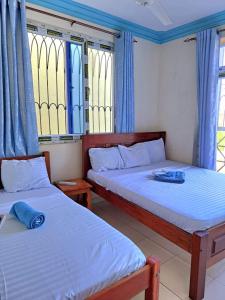 two beds in a room with blue curtains and windows at Bamburi Mombasa two bedroom Cutraz homes apartments with swimming pool 005 in Mtwapa