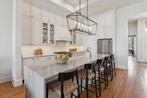 a kitchen with white cabinets and a large island with bar chairs at New Luxury Home Heated Pool & Spa in New Orleans +35 photos