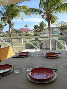 a table with red plates and glasses and palm trees at Grain de Corail in Saint-François