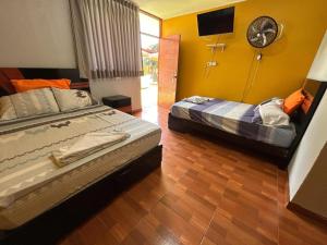 two beds in a room with yellow walls and a fan at Hospedaje Los Pecanos in Ica