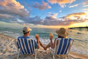 a man and woman sitting on the beach with drinks at Amazing Sunsets Steps to Pier Park Heated Pool Hot Tub in Panama City Beach +68 photos